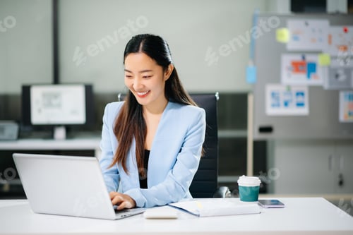 Preview: Asian woman using laptop and tablet while sitting at her working place. Concentrated in office