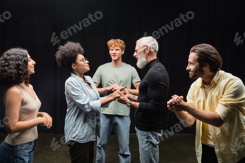 Preview: bearded art director holding hands with african american actress near students in theater school.