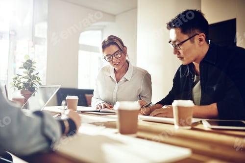 Preview: Smiling coworkers discussing paperwork at a table in an office