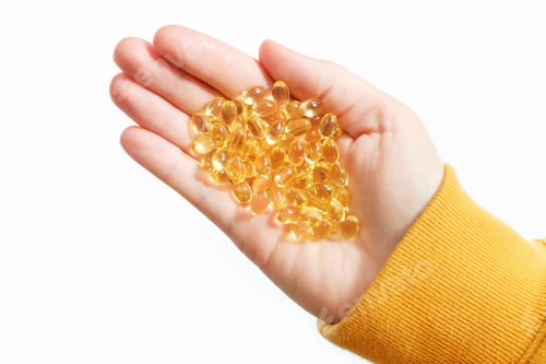 Visualização: Mão feminina segura cápsulas amarelas de vitamina D em fundo branco, vista superior de perto.