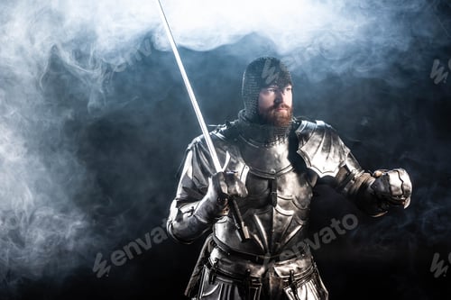 Preview: handsome knight in armor looking away and holding sword on black background