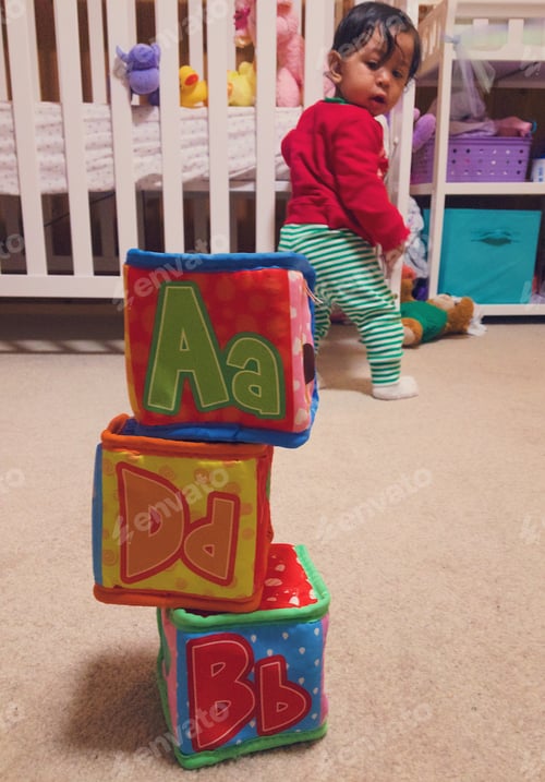 Preview: Diverse baby girl at home in room playing with educational alphabet blocks