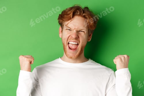 Preview: Close-up of lucky young man winner, celebrating victory, shouting yes with joy and making fist pumps