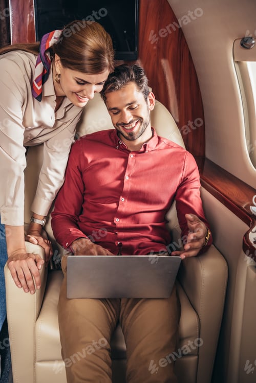 Preview: smiling boyfriend and girlfriend looking at laptop in private plane