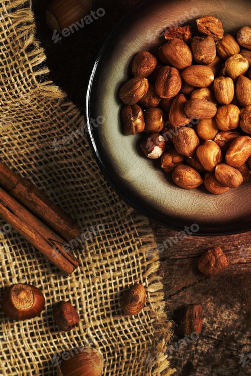 Preview: Close-up image of a bowl with peanuts and cinnamon sticks placed on a wooden table