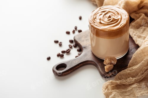 Preview: Delicious Dalgona Coffee in Glass on Wooden Cutting Board With Brown Sugar Near Coffee Beans, Cloth