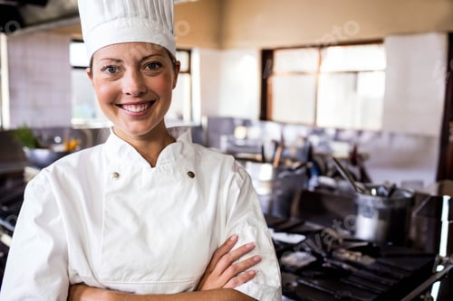 Preview: Female chef standing in restaurant kitchen crossing arms near stainless steel stations, copy space