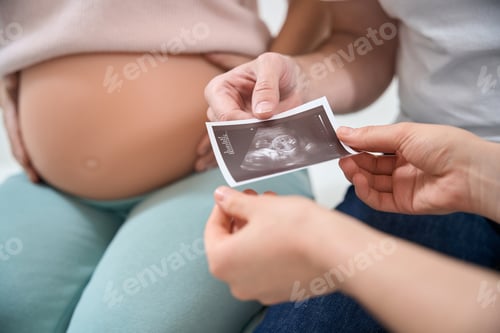 Preview: Close-up man holding the ultrasound picture of his baby in wife's womb