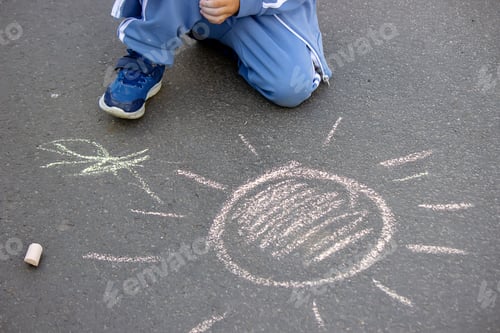 Preview: Cute little child draws the sun with chalk outdoors, summer time, chalk. Selective focus.