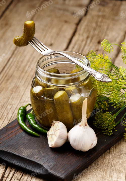 Preview: Open jar with pickled cucumbers and cucumber on a fork on a wooden background.