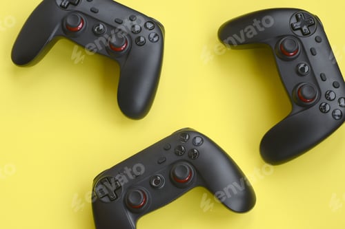 Preview: Three modern black gamepads on yellow background close up