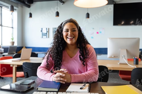 Preview: Portrait of happy biracial young businesswoman sitting at desk in creative office