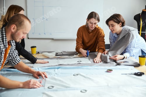 Preview: Woman tailor showing fabric sheet to co-worker while cutting