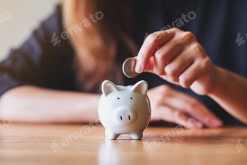 Preview: Closeup image of a woman putting coin into piggy bank for saving money concept