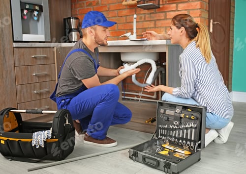 Plumber Repairing Sink for Woman in Kitchen