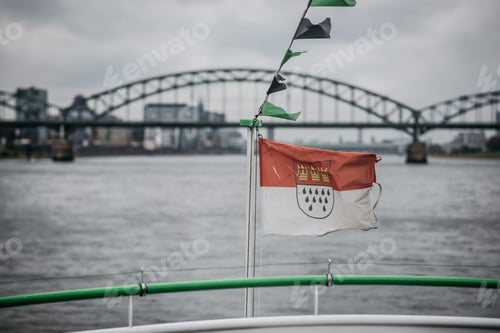Preview: Tranquil body of water is in the foreground with a flag of Cologne waves proudly in the breeze