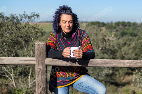 Preview: Mature woman enjoying coffee break outdoors by fence