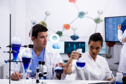 Preview: Female scientist in white coat holding a test tube with blue solution