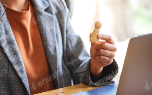 Preview: Businesswoman leader holding and choosing wooden people while working on laptop computer in office