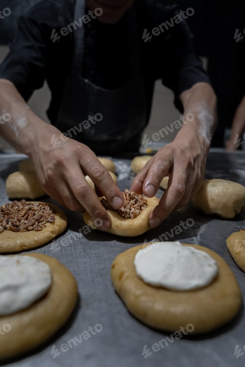 Preview: A young Hispanic baker is stuffing dough buns with nuts