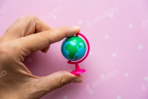 Preview: Small toy globe in woman hand on a pink background