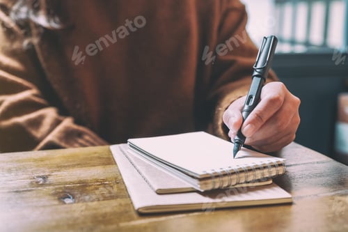 Preview: Closeup image of a woman writing on blank notebook with fountain pen on wooden table