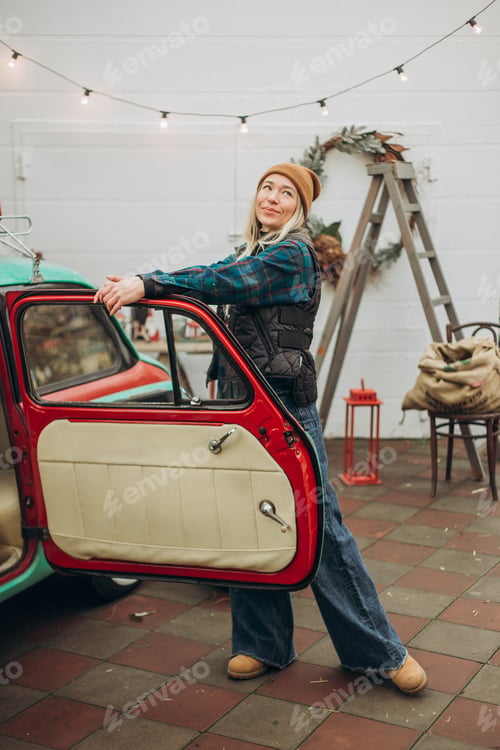 Preview: Young blonde woman near retro car with Christmas decorations