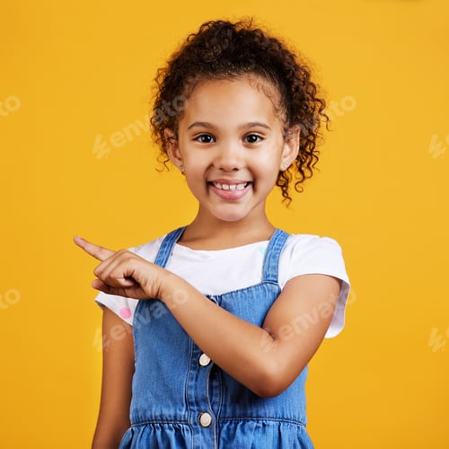 Preview: Studio portrait mixed race girl pointing sideways towards copyspace isolated against a yellow backg