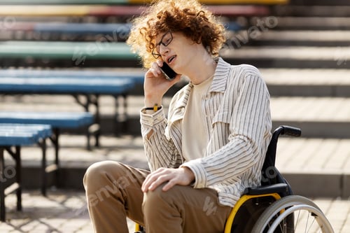 Preview: Curly, red-haired guy in glasses sits in a wheelchair and talks on a mobile phone.