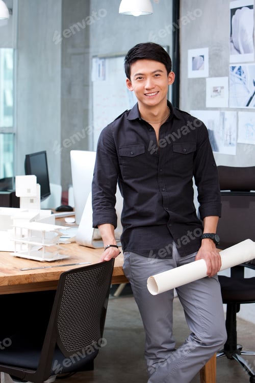 Preview: Male architect holding blueprint in studio