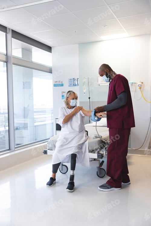 Preview: African american doctor measuring blood pressure of senior caucasian patient with prosthetic leg