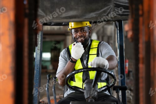 Preview: Smiling African American male worker driving forklift truck in heavy metal industrial factory.