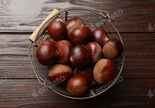 Preview: Sweet fresh edible chestnuts in metal basket on wooden table, top view