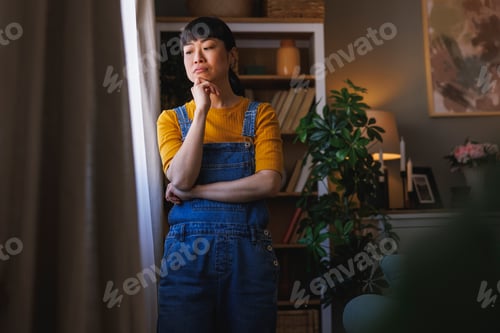 Preview: Pensive woman standing by the window and relaxing at home