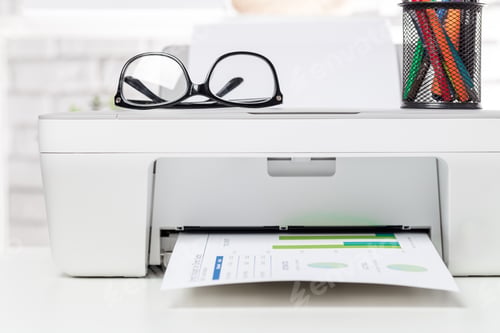 Preview: Printer producing financial report on desk with glasses and pen holder during daylight