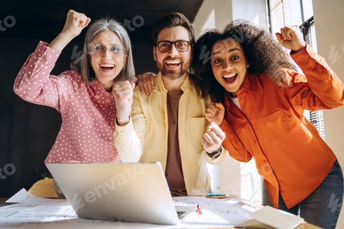 Preview: Group of excited architects celebrating success on laptop in office