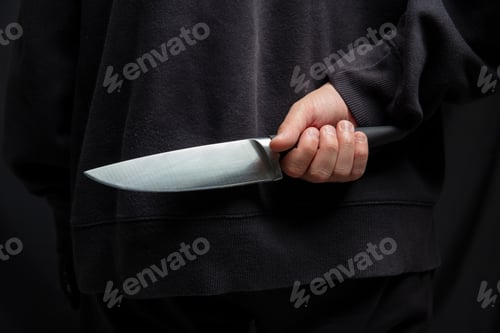 Preview: Robber hiding a knife behind his back, man holding a weapon in hand closeup