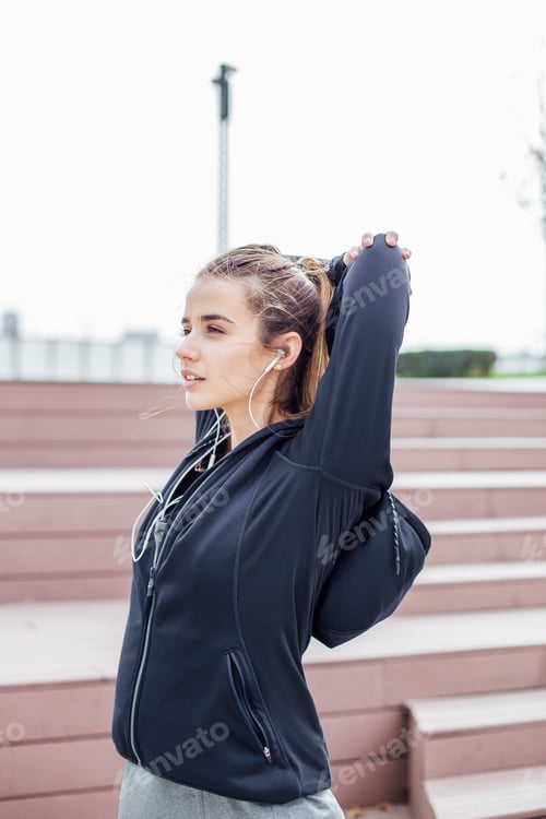 Preview: Fit young woman with earphones doing stretching exercises on stairs outdoors