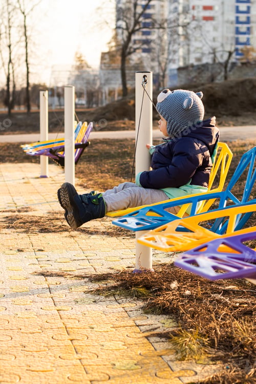 Preview: A little child rides on a colorful swing in a city park at sunset