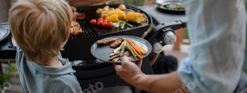 Preview: Father putting grilled meat and vegetable on plate to his son during family summer garden party.