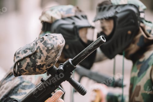 Preview: selective focus of marker gun in hand of paintball player standing face to face with other player