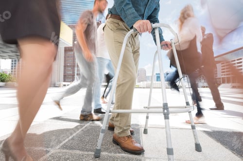 Preview: A man with a walking frame between a crowd of people in a city