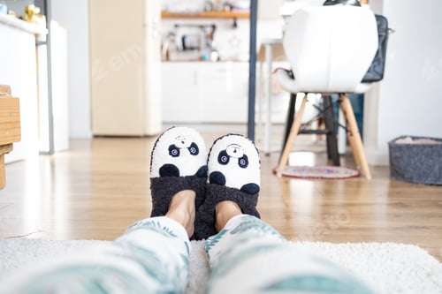Preview: Young woman in soft funny slippers at home on wooden floor.