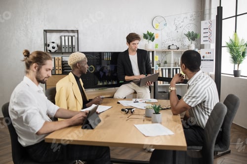 Preview: Male company worker in formal wear sitting at office desk and listening to team leader.