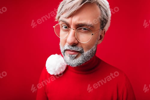 Preview: Old man in red shirt posing in christmas day. Grey-haired male model in santa claus hat and glasses
