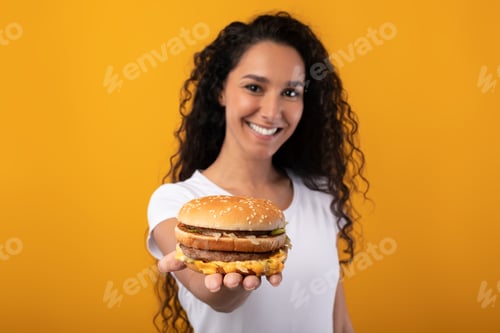 Preview: Happy Young Lady Holding And Giving Burger At Studio