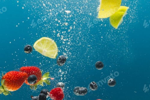 Vista previa: Close up of berries, lime and lemon slices falling into water with copy space on blue background