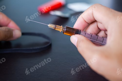 Preview: Hand holding heroin in syringe with rubber band, old spoon and cigarette lighter.