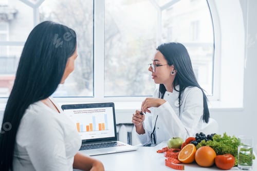Preview: Female nutritionist with laptop gives consultation to patient indoors in the office