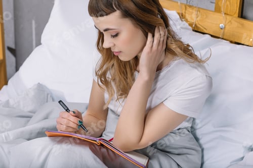 Preview: girl writing something to notebook in bed in morning